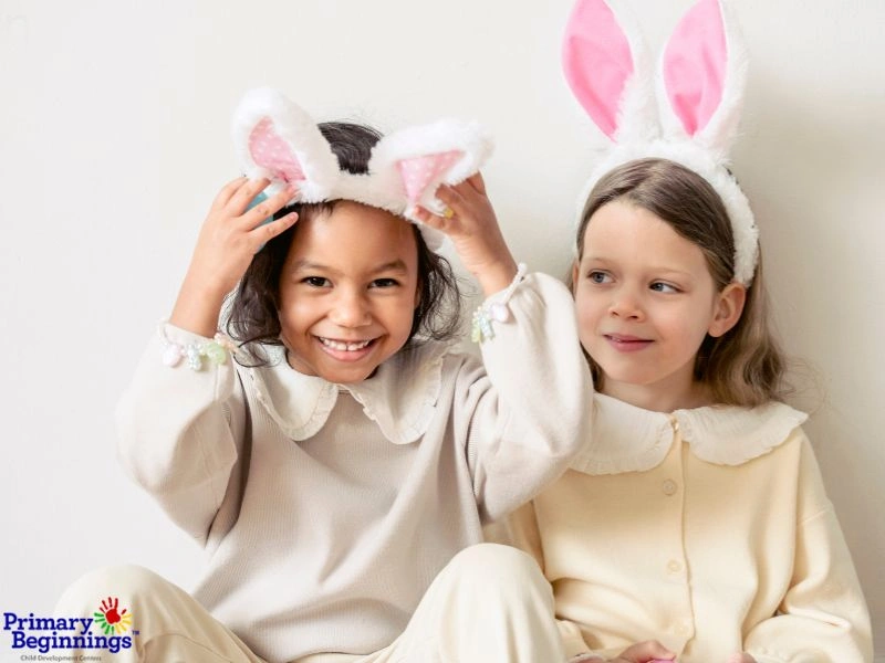 Two young girls wearing bunny ears and neutral color dresses. 