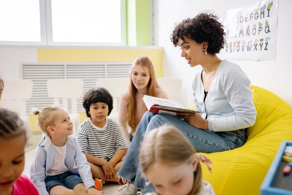 Woman sitting on a beanbag and reading to a group of children in a classroom.
